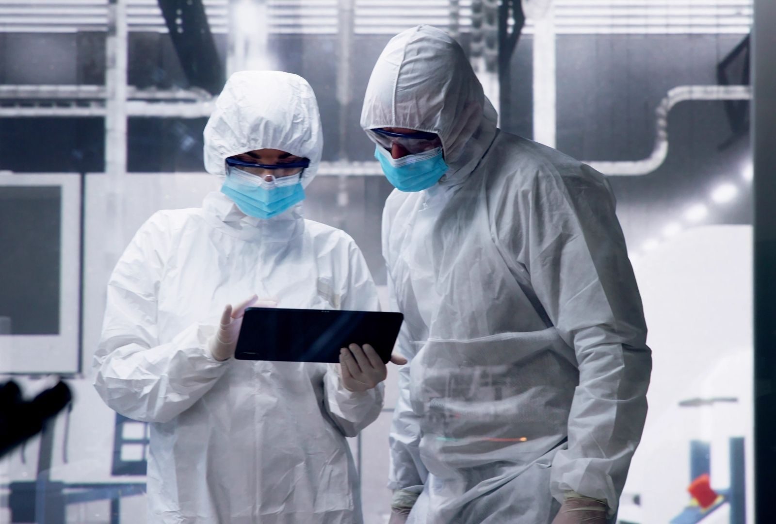 Two cleanroom workers in protective suits reviewing a tablet in a semiconductor fab