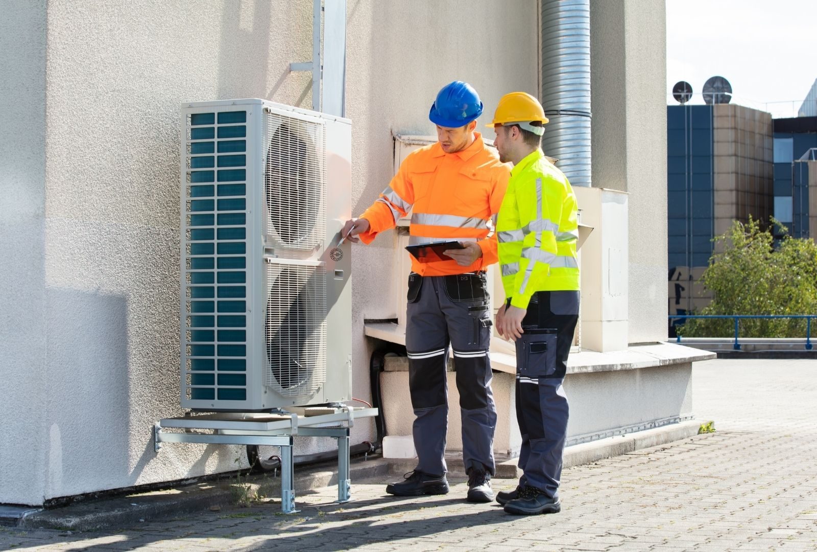 Two technicians in hard hats and high-visibility gear servicing an outdoor HVAC unit